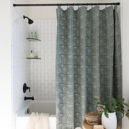 Sage green shower curtain with geometric damask pattern hung from black rod in white tile bathroom.