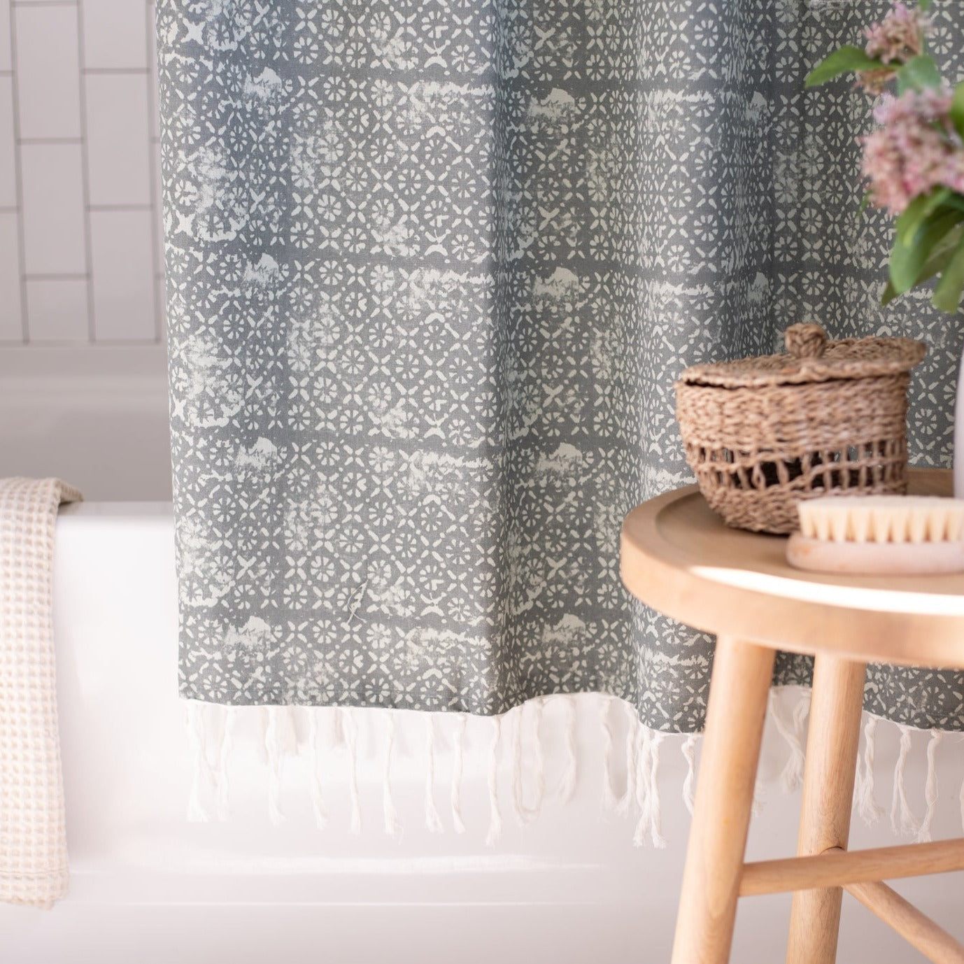 Gray and white geometric patterned shower curtain with white fringe trim hung in a bathroom.