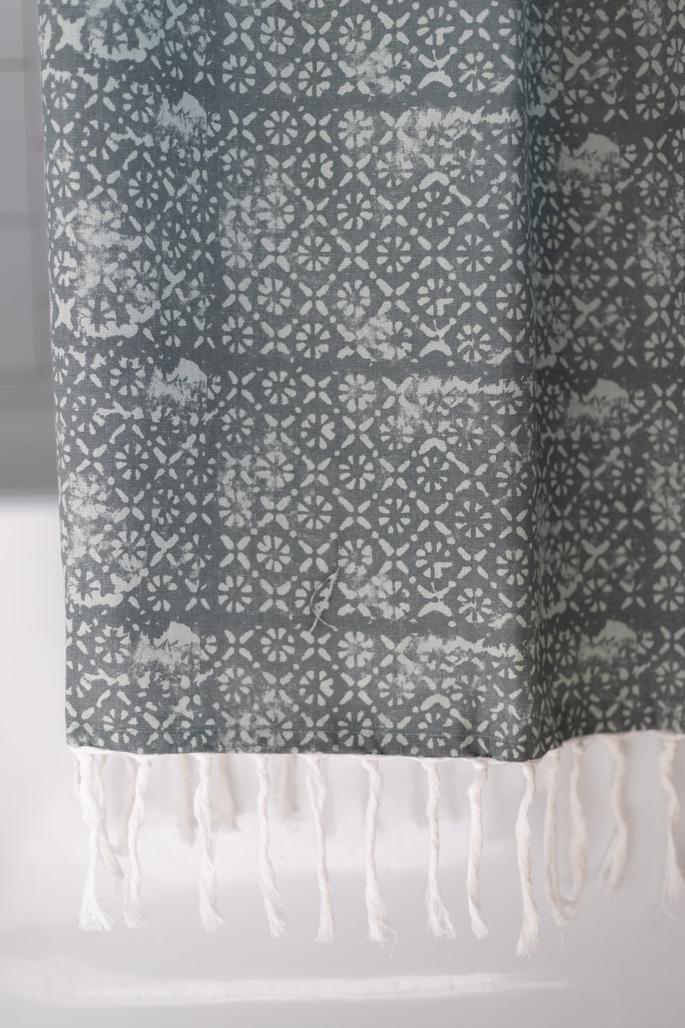 Gray and white geometric patterned shower curtain with white fringe trim at bottom.