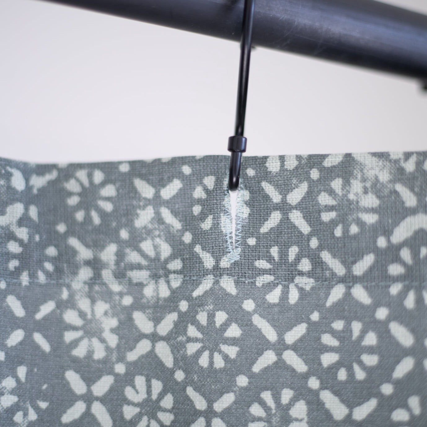 Gray shower curtain with white floral and dot pattern, hung on black rod with plastic ring.