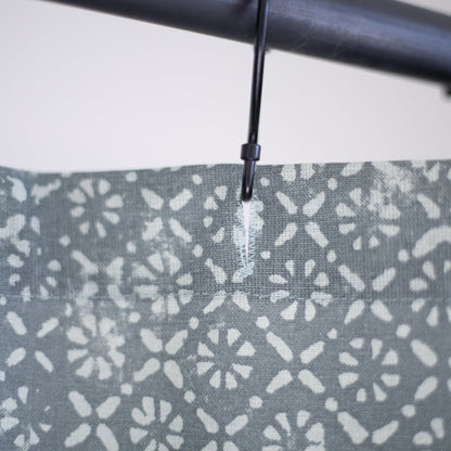 Gray shower curtain with white floral and dot pattern, hung on black rod with plastic ring.