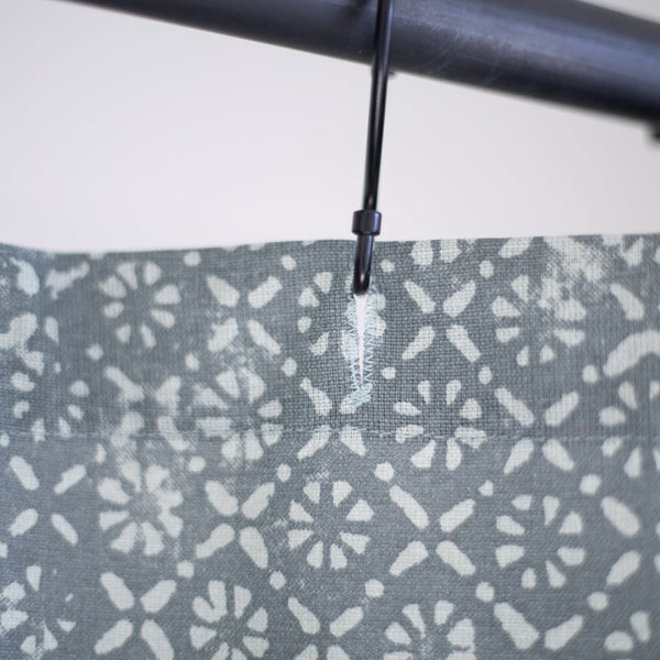 Gray shower curtain with white floral and dot pattern, hung on black rod with plastic ring.