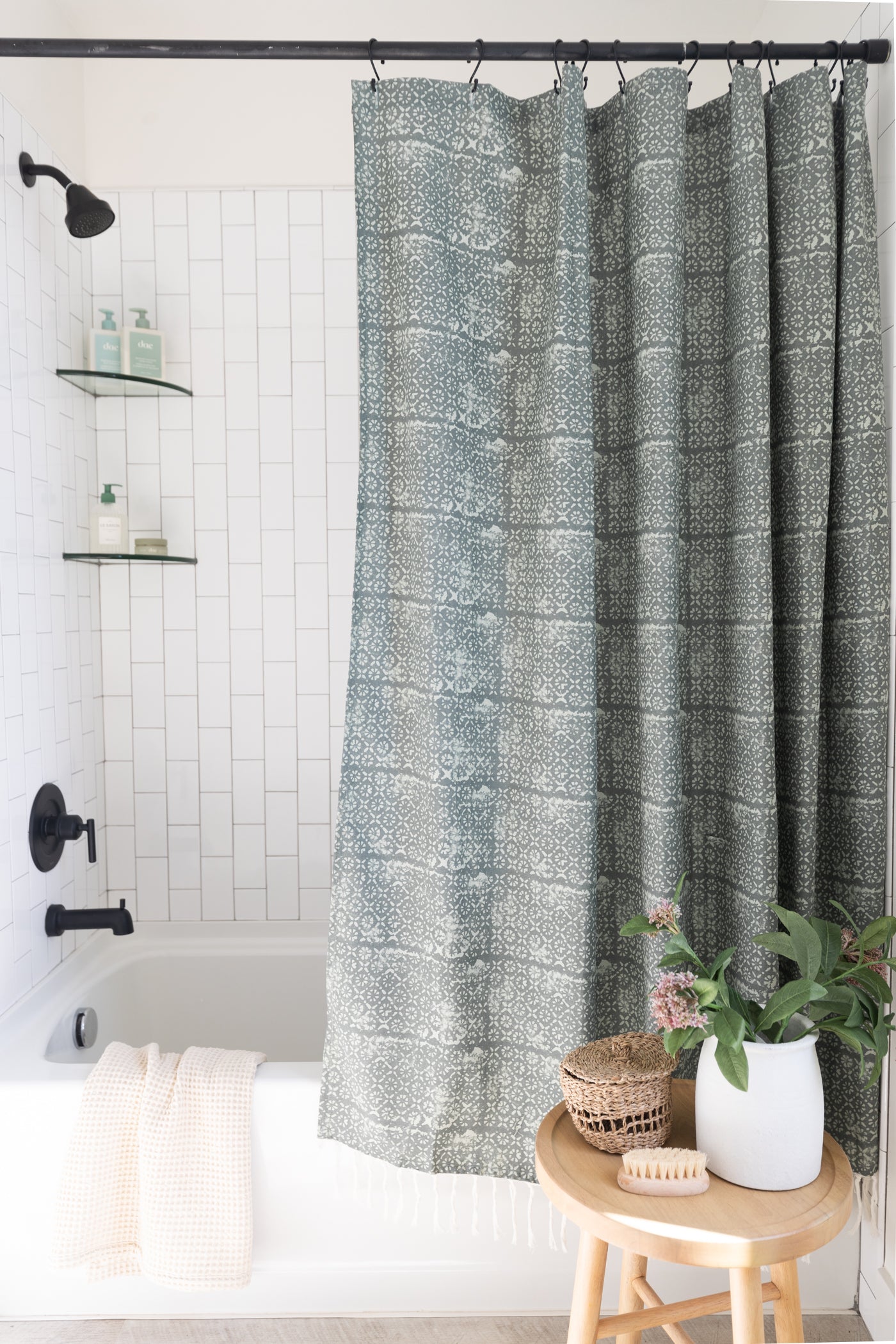 Gray and cream damask patterned shower curtain hung from black rod with hook rings in white tile bathroom.