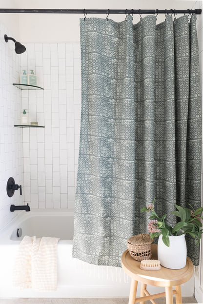 Gray and cream damask patterned shower curtain hung from black rod with hook rings in white tile bathroom.