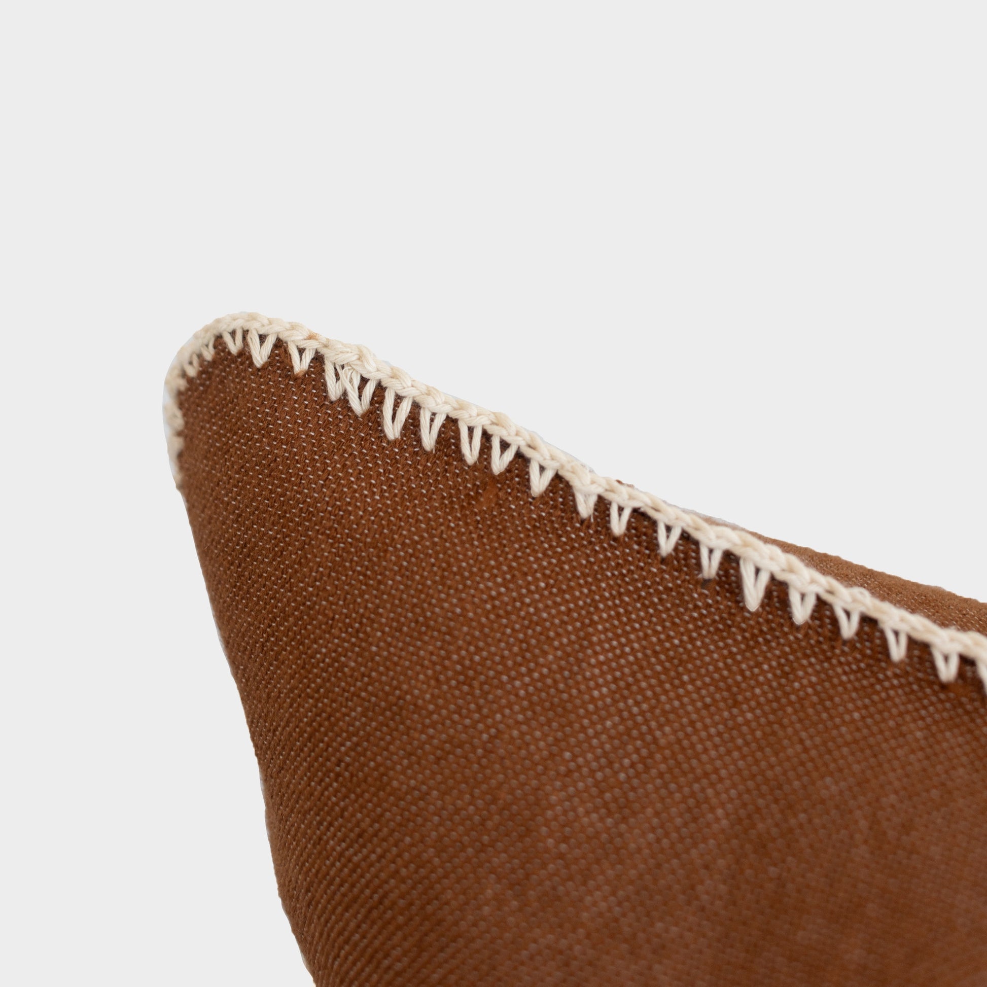 Brown cushion with cream whipstitched edge trim and textured fabric surface.