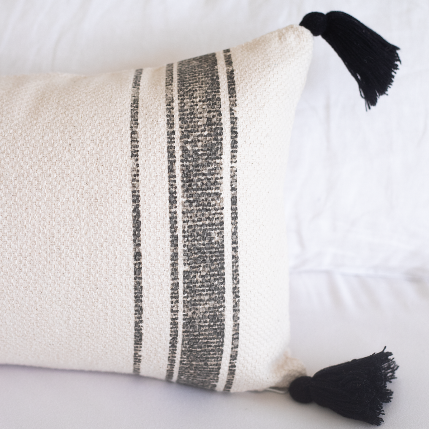 Cream lumbar pillow with charcoal stripes and black tassels on corners.