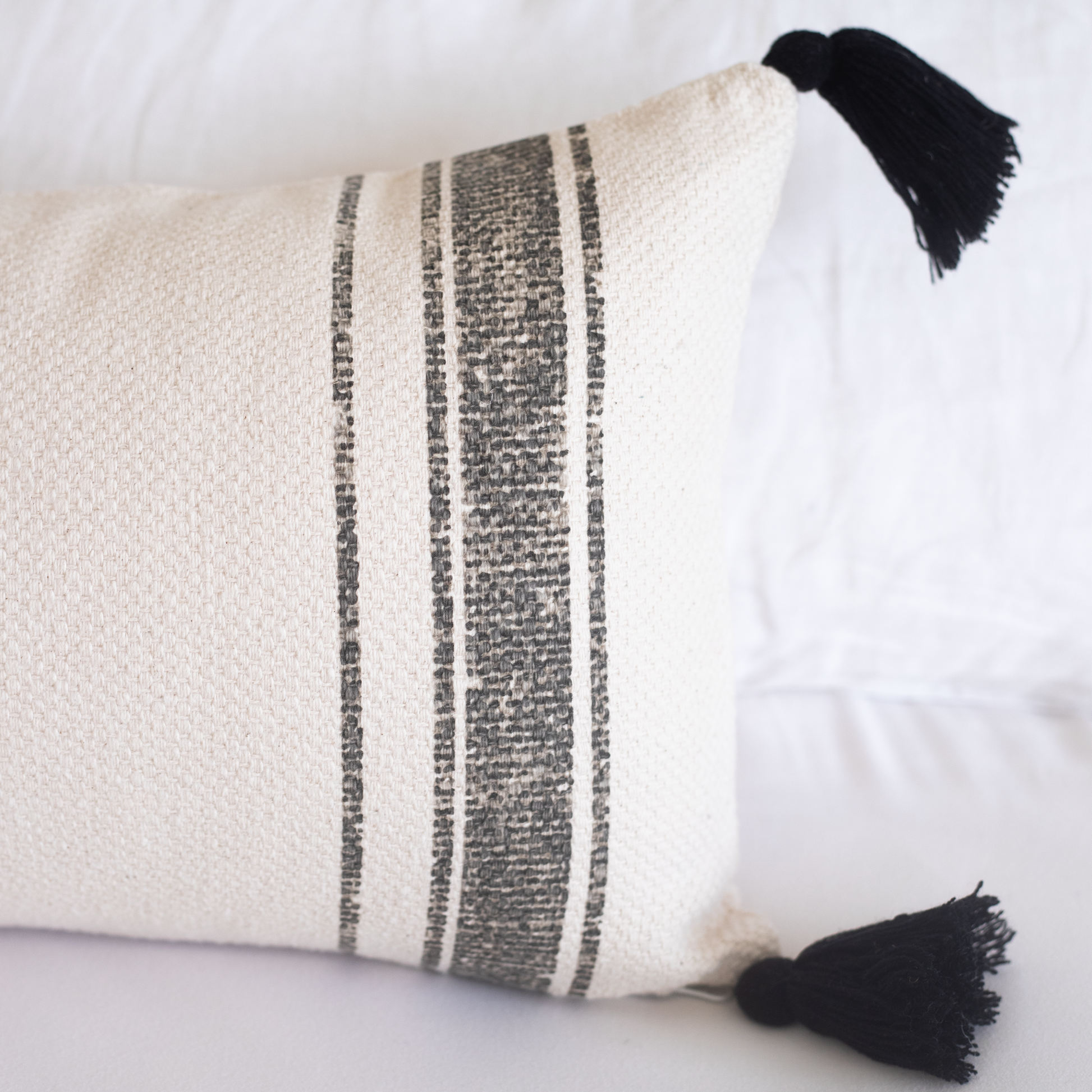 Cream lumbar pillow with charcoal stripes and black tassels on corners.