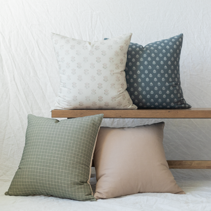 Four decorative pillows in cream, charcoal, sage green, and taupe with various patterns arranged on wooden shelf.