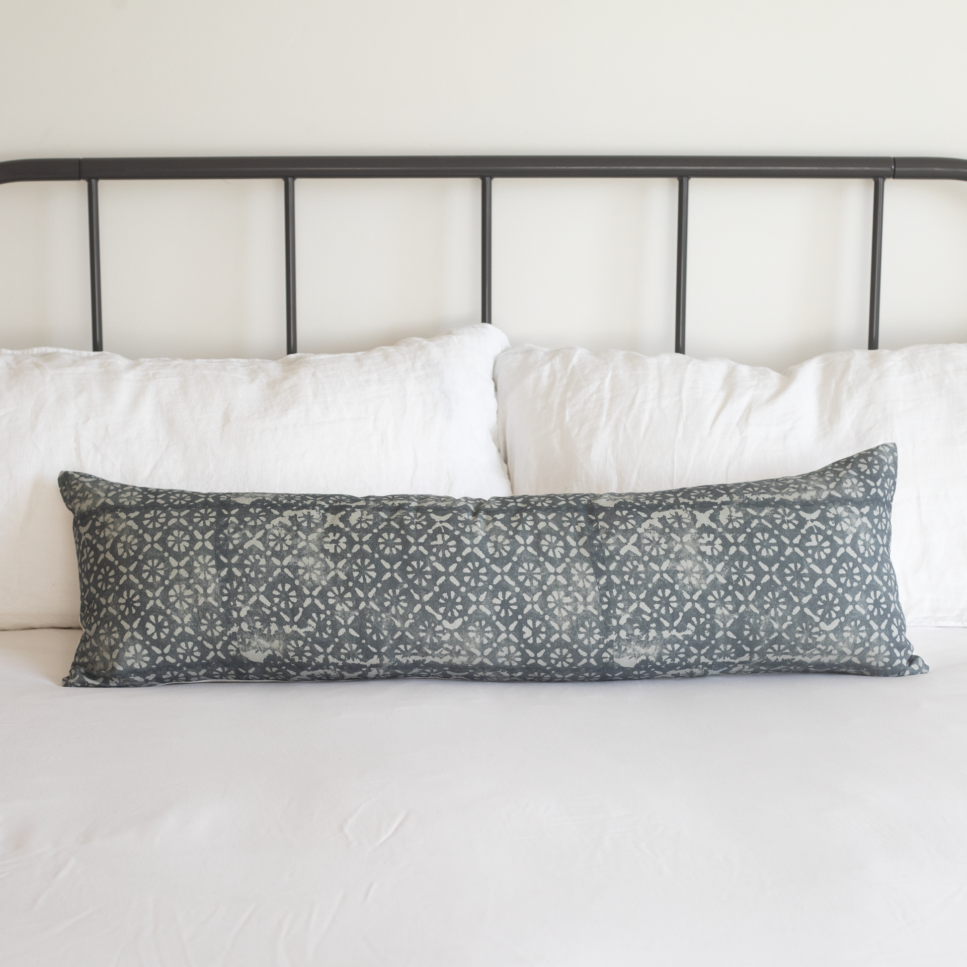 Gray lumbar pillow with diamond floral pattern displayed on white bedding against a black metal headboard.
