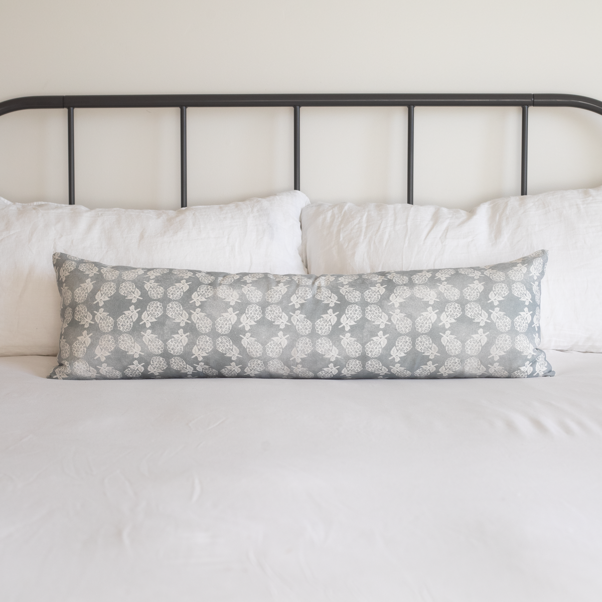 Long lumbar pillow with gray and white leaf print pattern on bed with black metal headboard and white bedding.