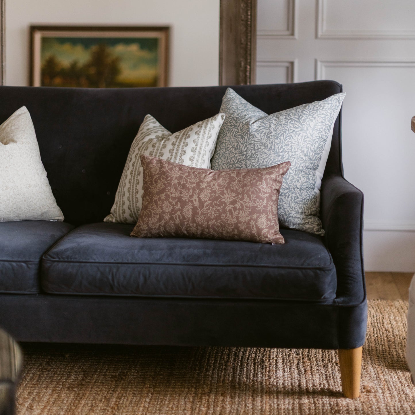 Dark blue sofa with four patterned throw pillows in cream, beige, gray, and mauve tones arranged on seat.
