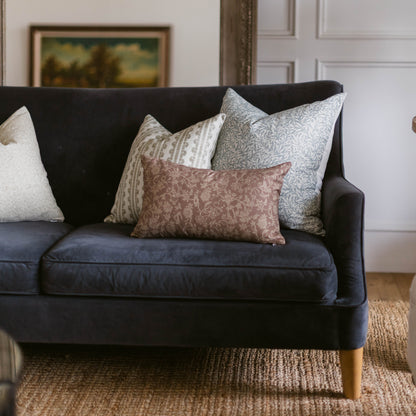 Dark blue sofa with four patterned throw pillows in cream, beige, gray, and mauve tones arranged on seat.