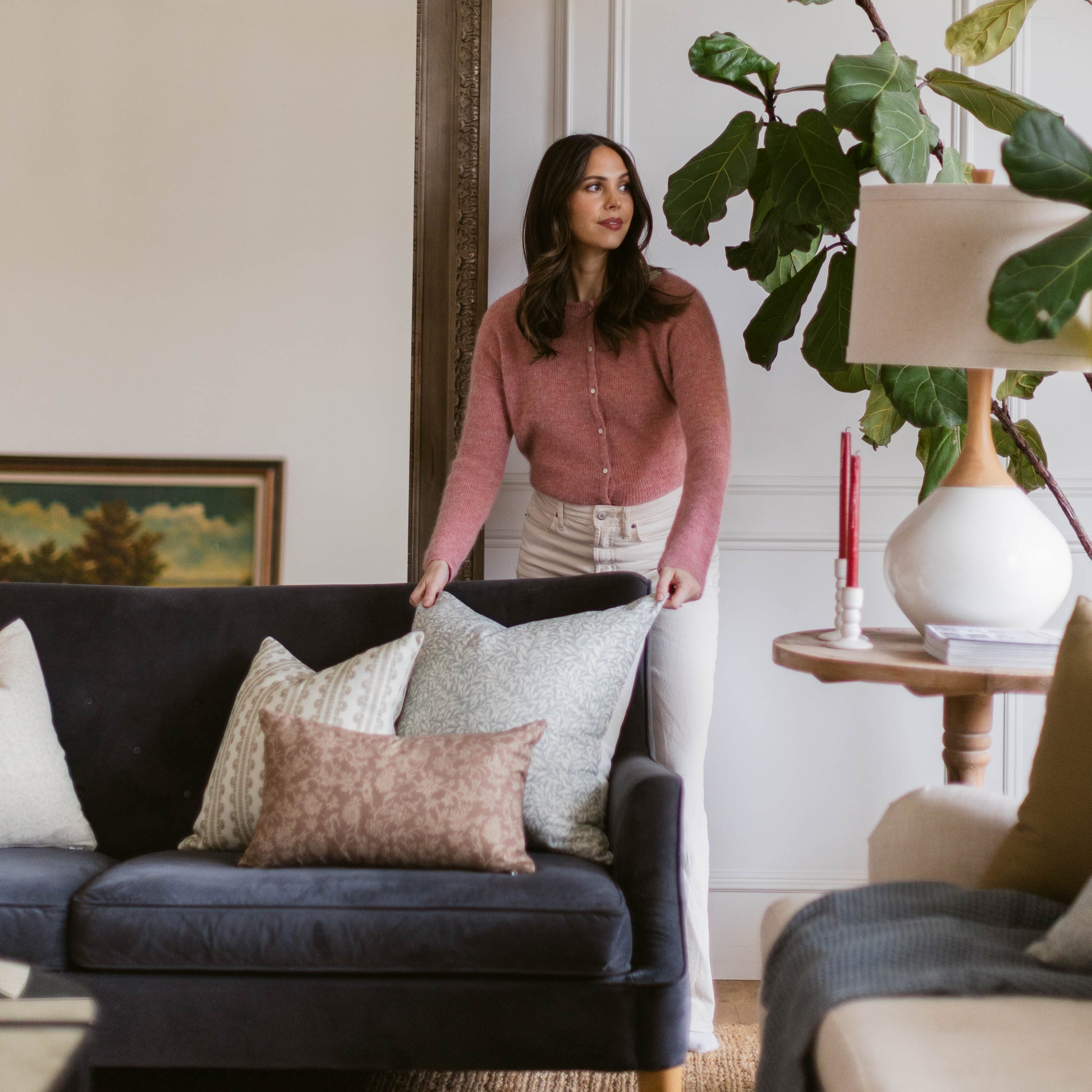 Woman standing beside dark upholstered sofa with decorative pillows in living room setting.