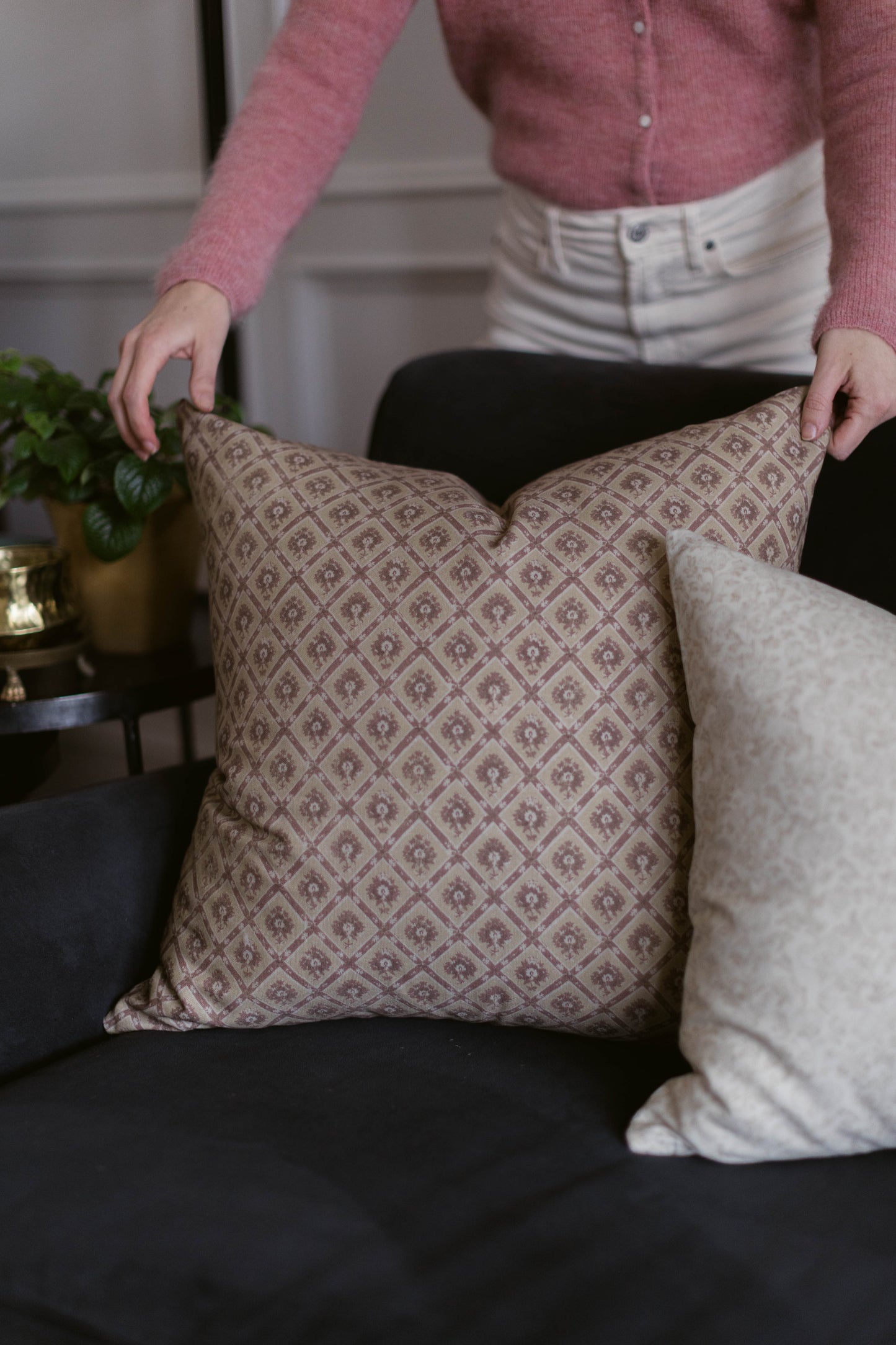 Taupe cushion cover with geometric diamond and floral pattern displayed on black sofa next to white textured pillow.