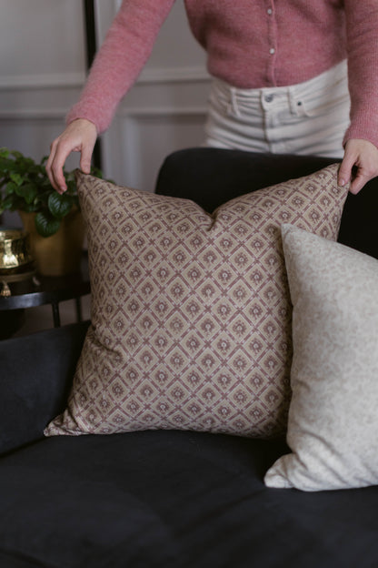 Taupe cushion cover with geometric diamond and floral pattern displayed on black sofa next to white textured pillow.