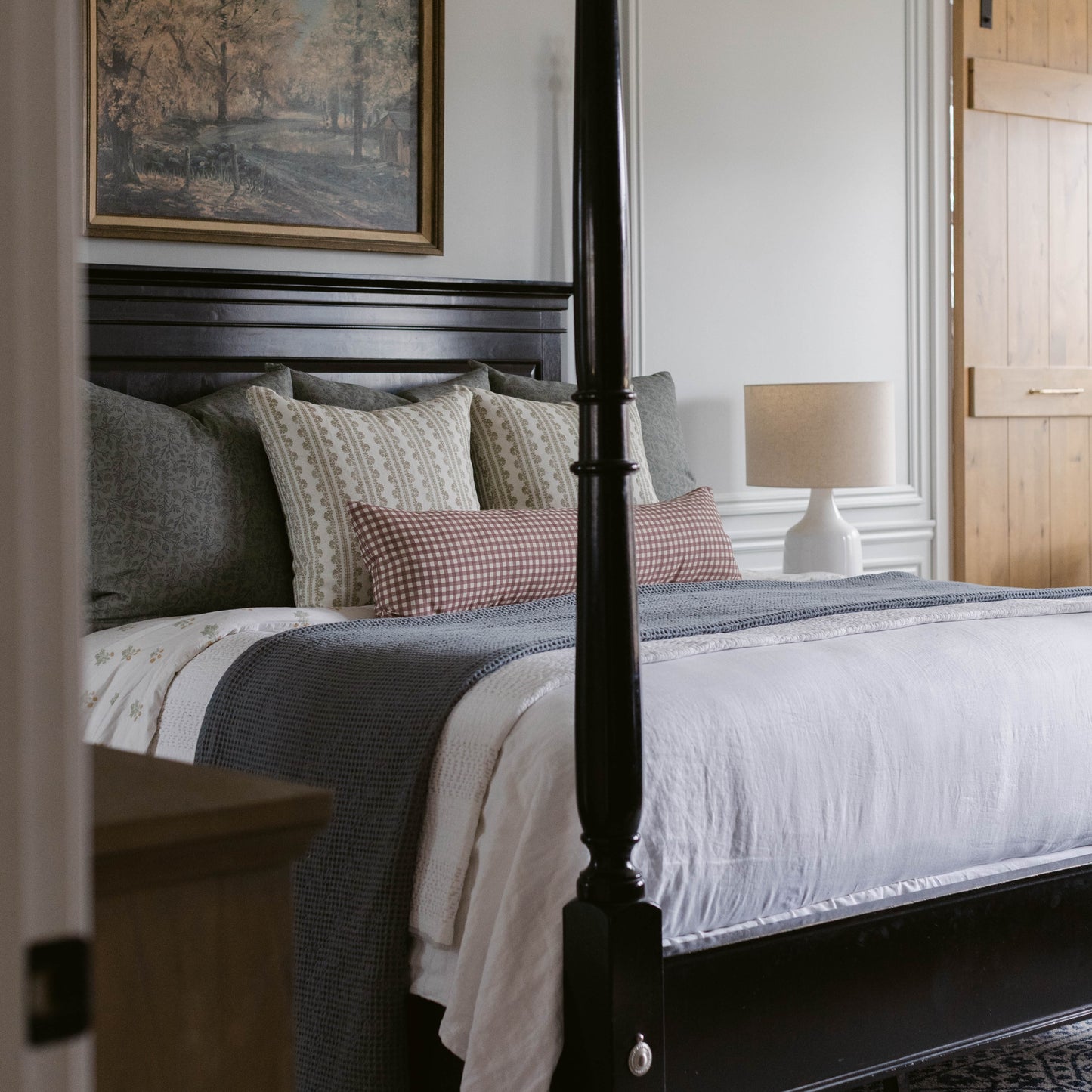 Striped linen pillow in cream and gray tones displayed on black four-poster bed with layered bedding.