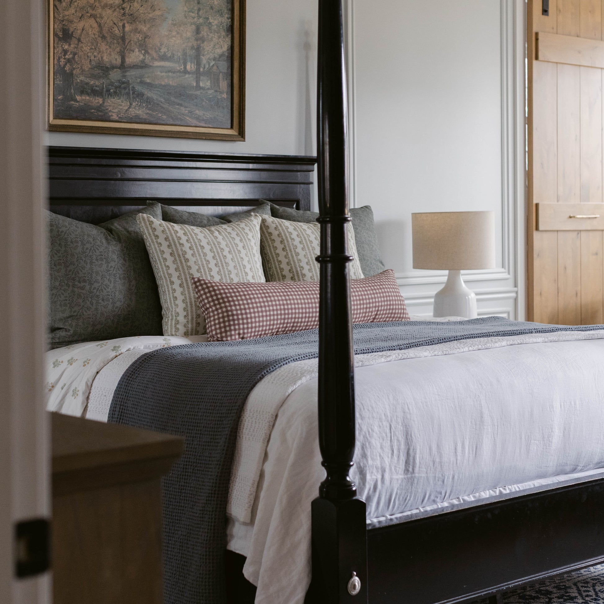 Striped linen pillow in cream and gray tones displayed on black four-poster bed with layered bedding.