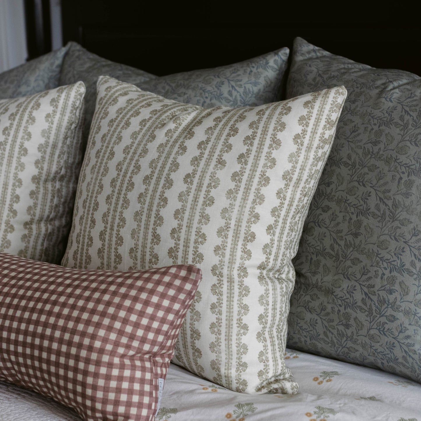 Linen pillow with vertical stripe and leaf pattern in cream and sage green, displayed with coordinating patterned pillows.