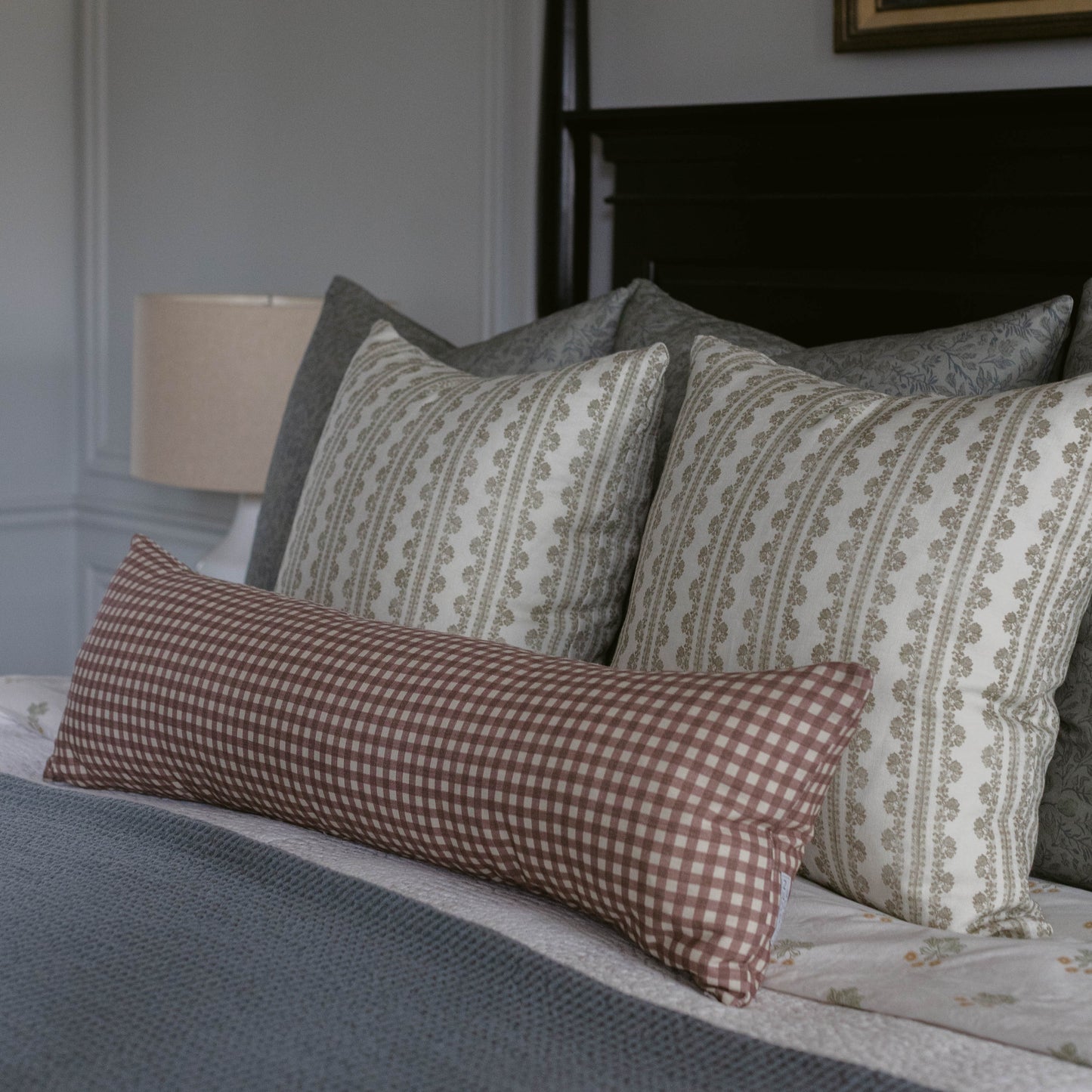 Rectangular linen pillow with red and white gingham pattern on front and coordinating striped pattern on back, displayed on b