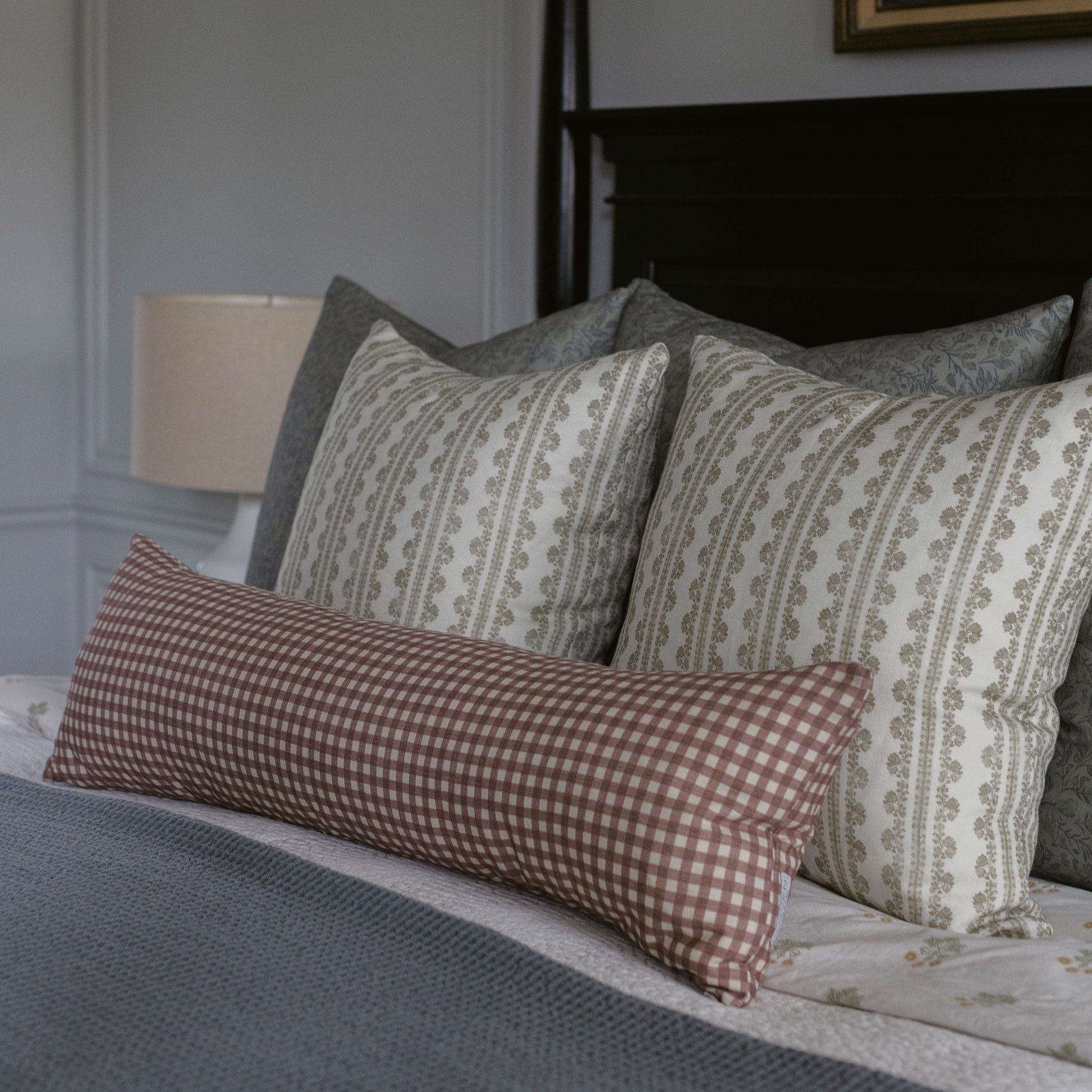 Rectangular linen pillow with red and white gingham pattern on front and coordinating striped pattern on back, displayed on b
