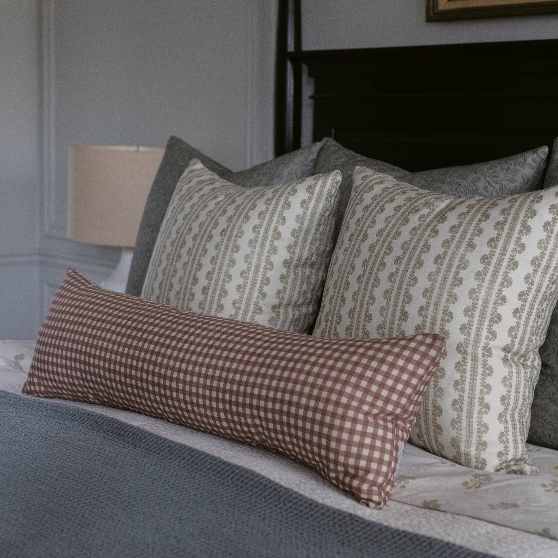Rose gingham patterned lumbar pillow with white checks displayed on a bed with striped pillows.