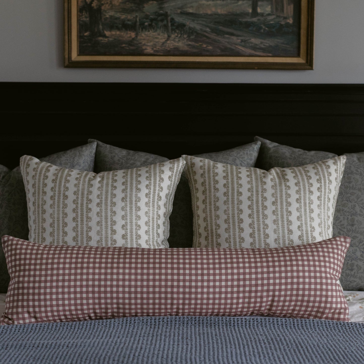 Rectangular linen pillow with mauve gingham pattern on one side and geometric stripe pattern on reverse, displayed on bed.