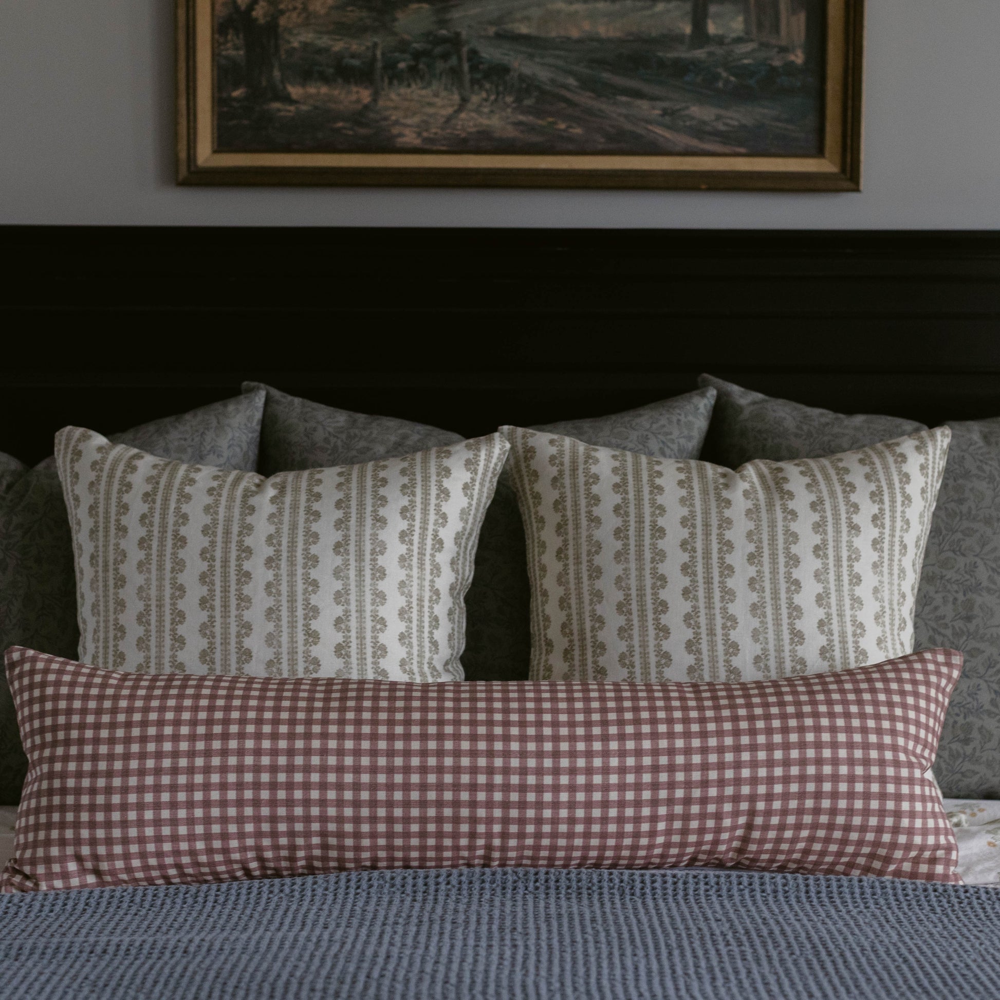 Rectangular linen pillow with mauve gingham pattern on one side and geometric stripe pattern on reverse, displayed on bed.
