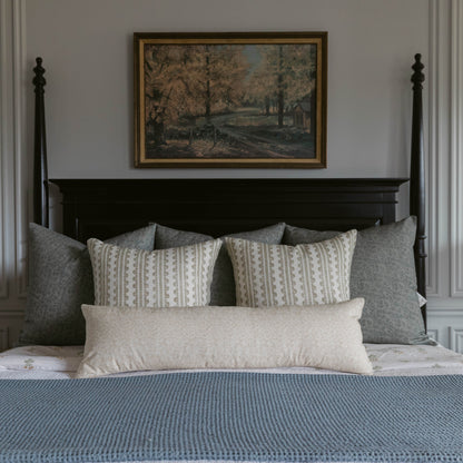 Cream lumbar pillow displayed on bed with patterned and gray pillows against black headboard.