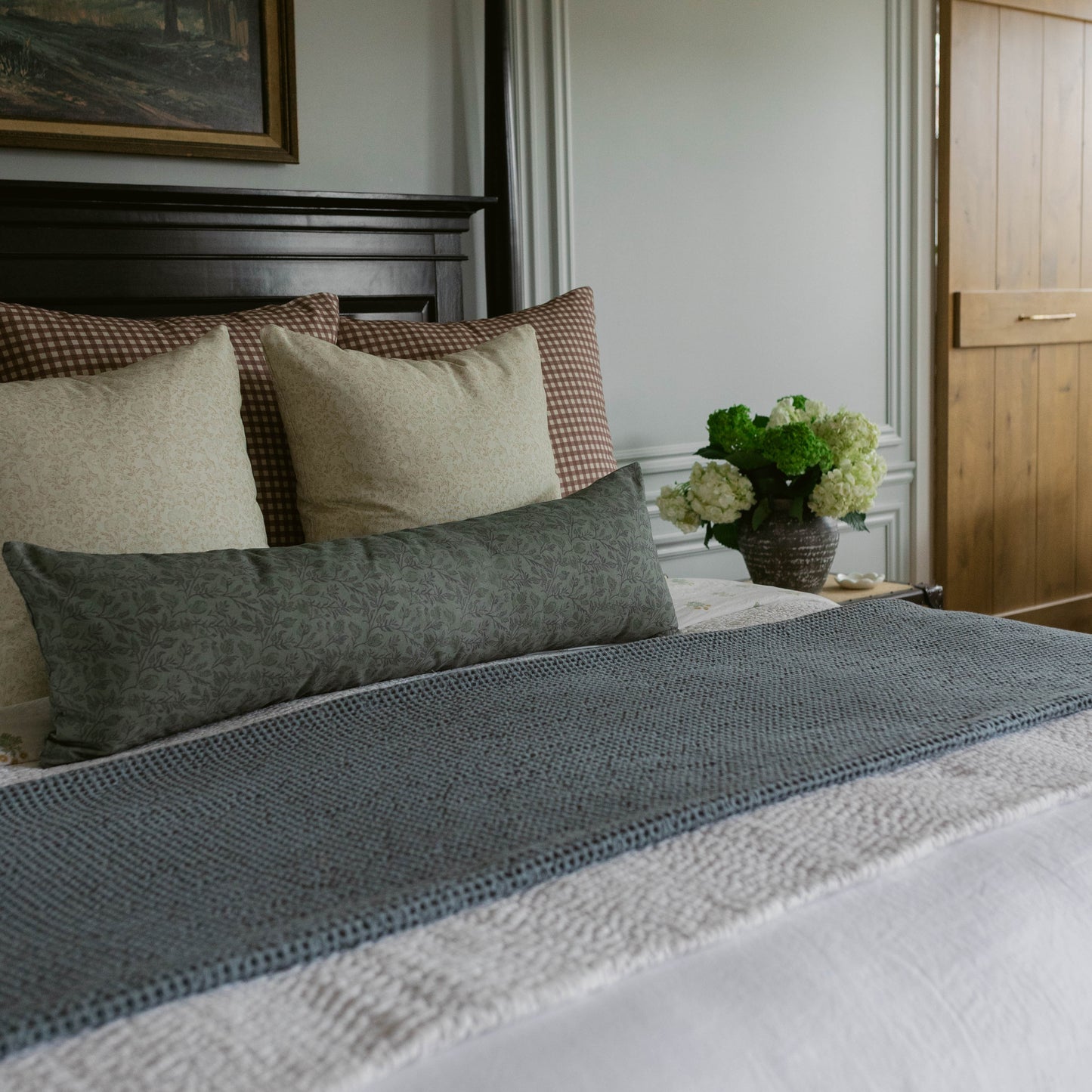 Blue horizontal striped bedding on made bed with layered pillows and nightstand with flowers.