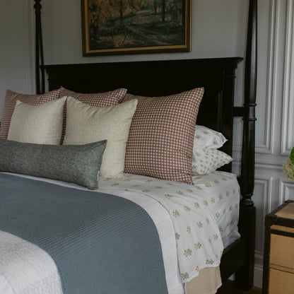 Decorative pillow with red and white gingham pattern displayed on bed with coordinating bedding and neutral textured pillows.
