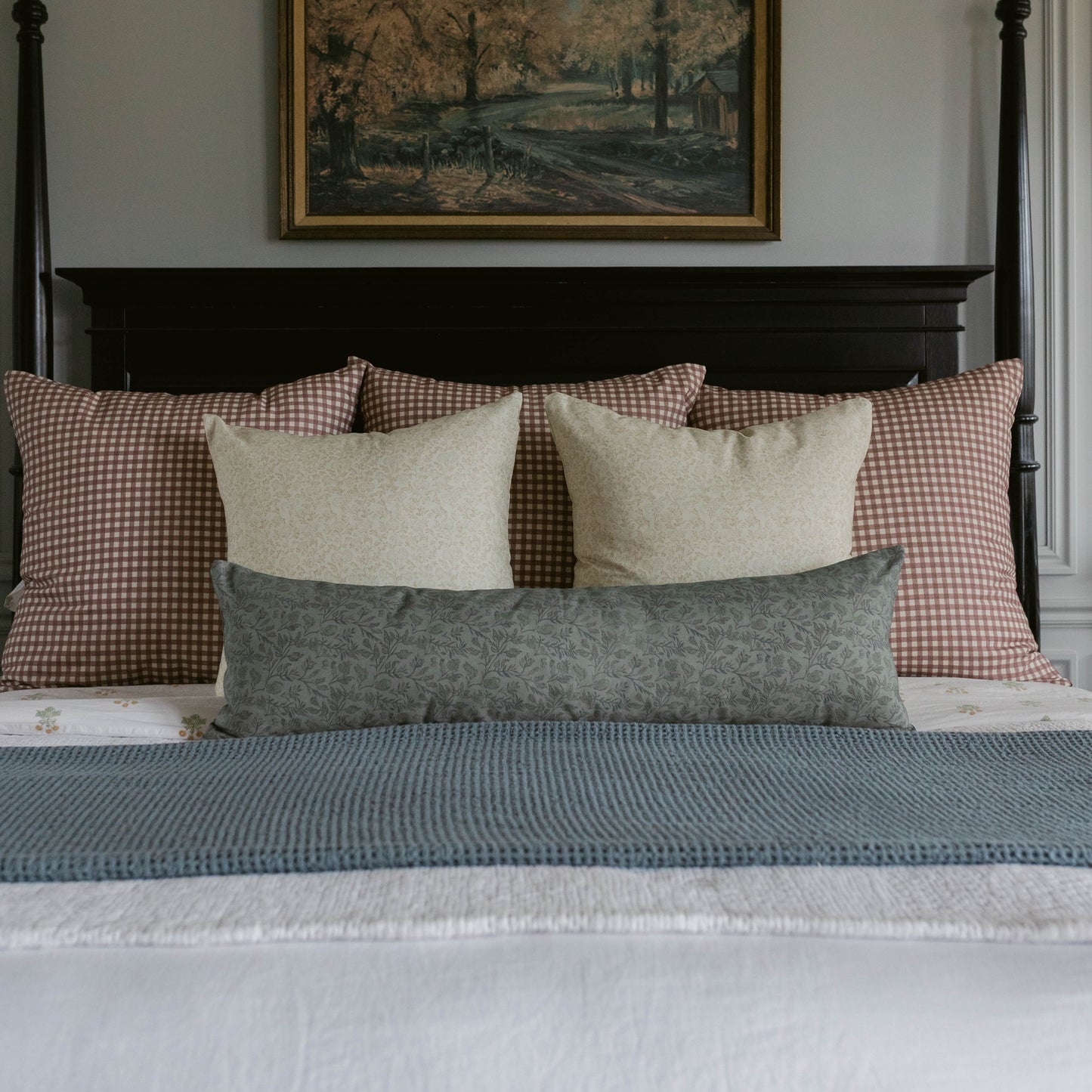 Blue-gray lumbar pillow displayed among cream and red gingham pillows on a bed with black headboard.