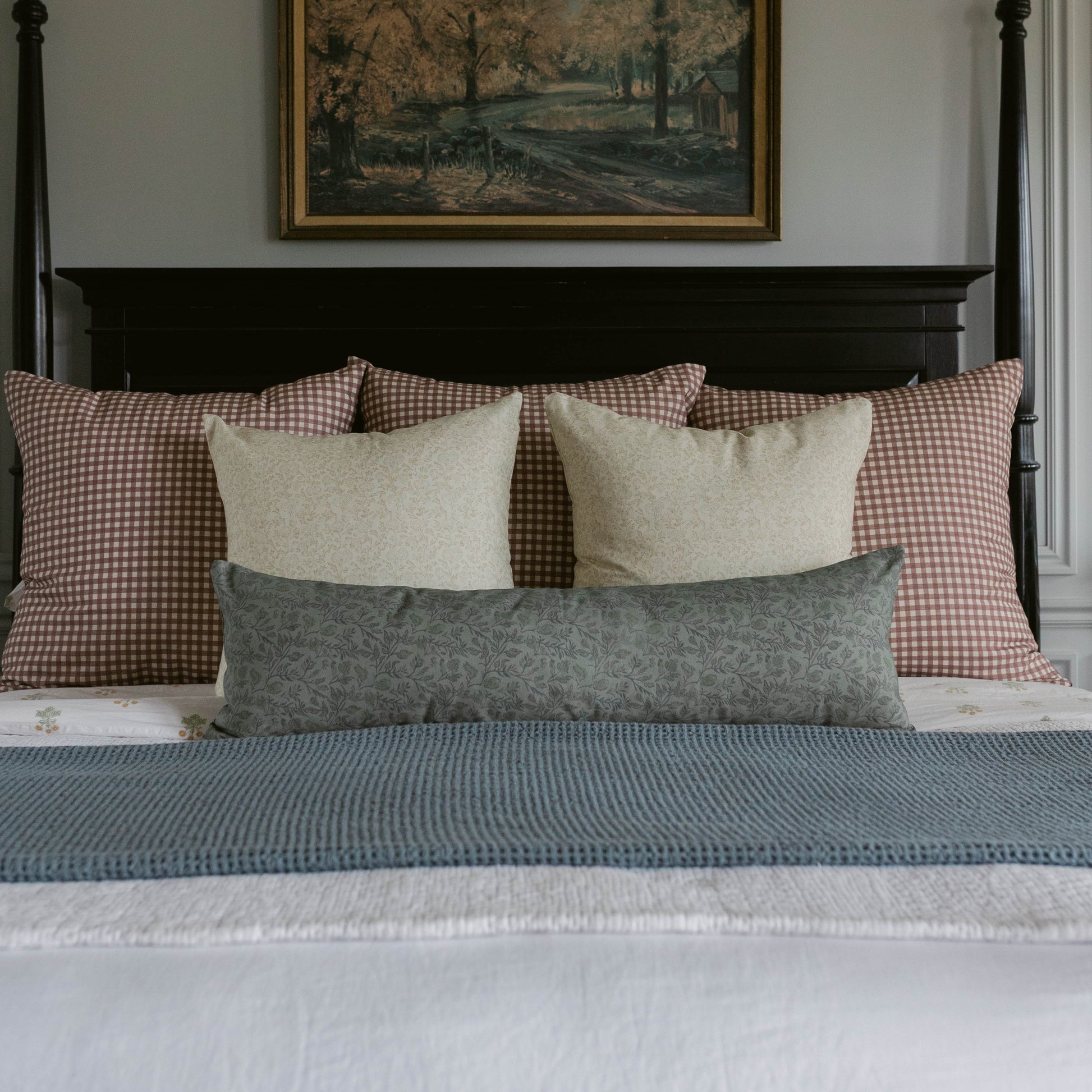 Blue-gray lumbar pillow displayed among cream and red gingham pillows on a bed with black headboard.