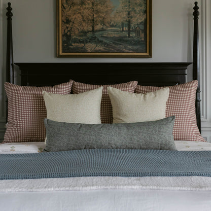 Bed styled with gray patterned lumbar pillow, cream rectangular pillows, and red gingham pillows against black four-poster be