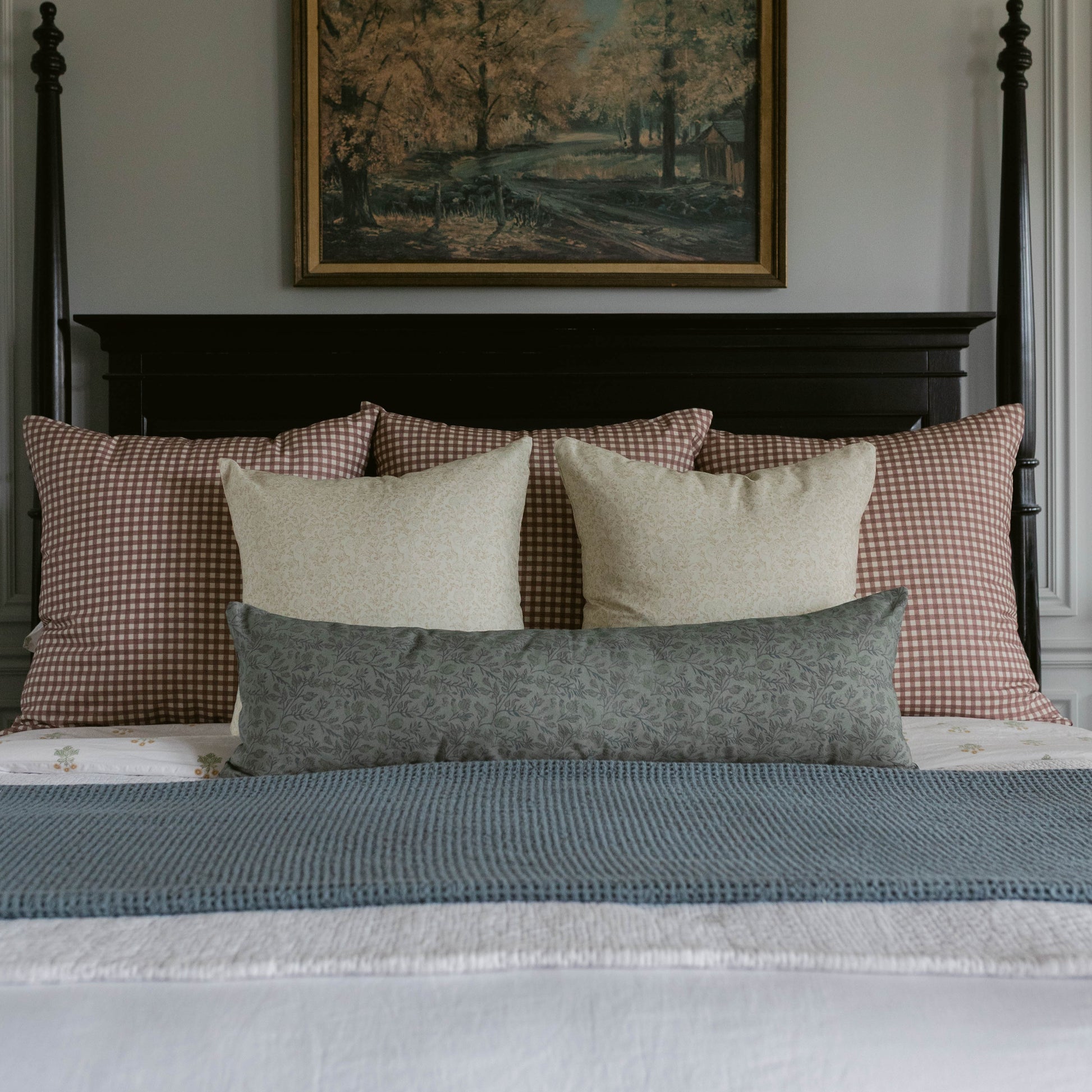 Rose gingham pillows in mauve and cream arranged on a black bed frame with neutral and patterned accent pillows.