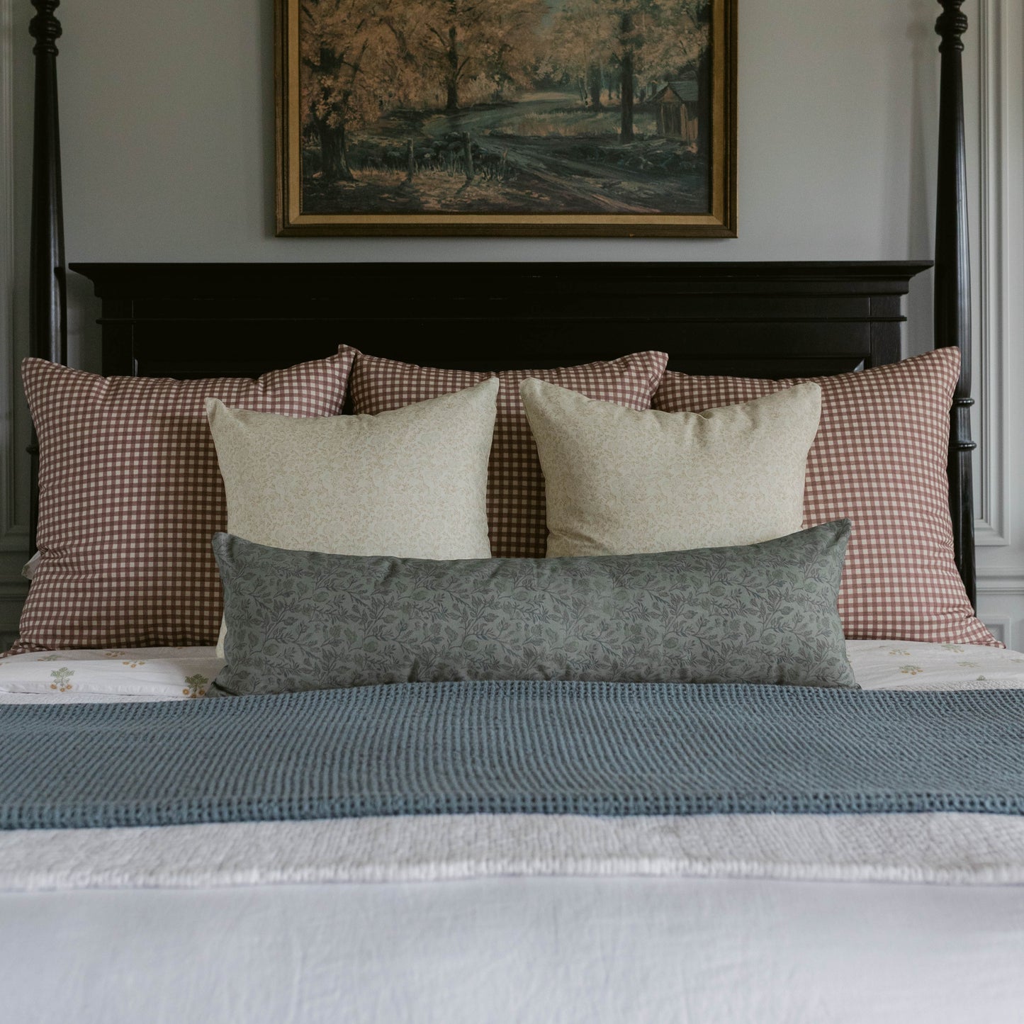 Rose gingham pillows in pink and white arranged on a bed with neutral and blue bedding.