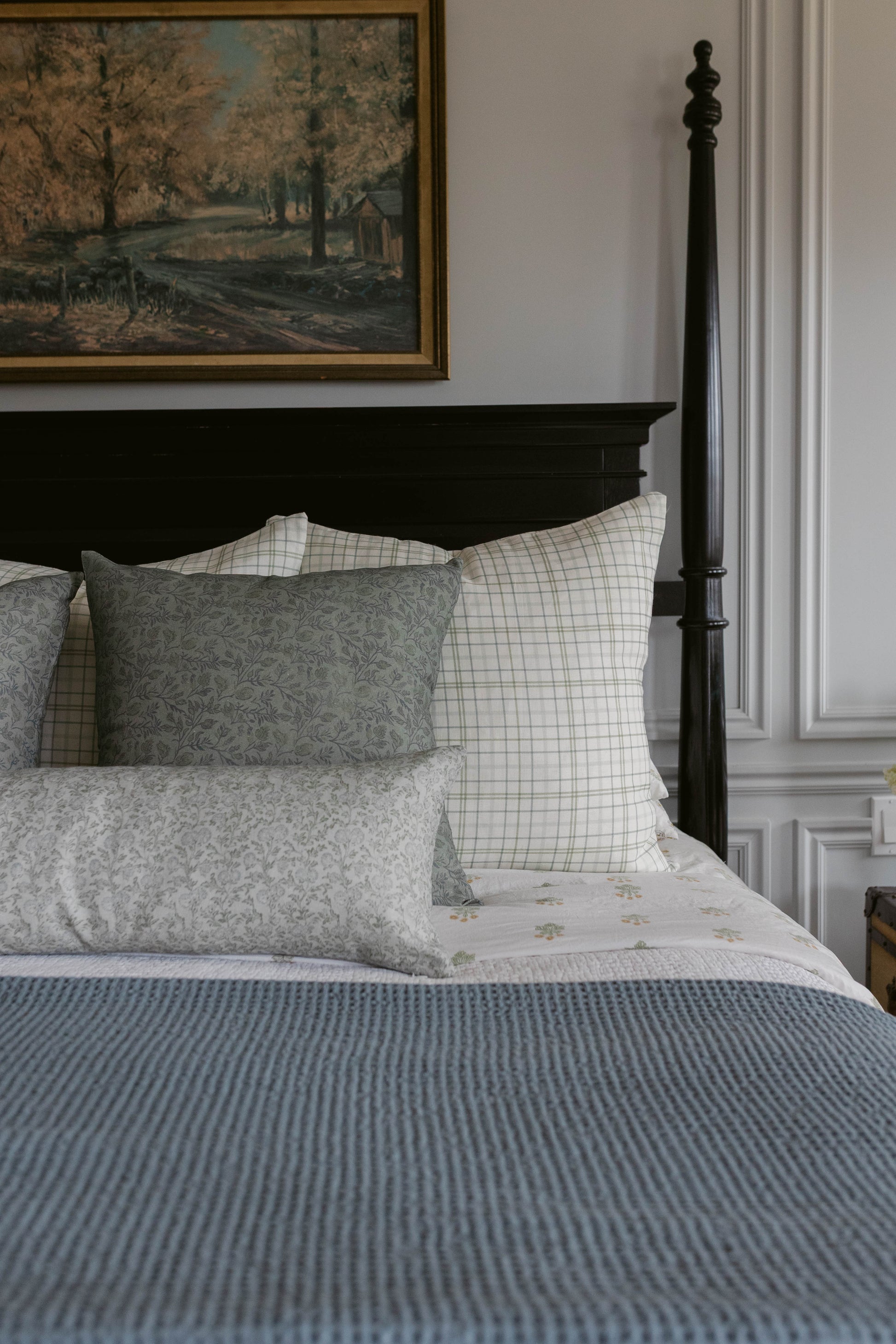 Grey and cream linen pillow with floral pattern displayed on bed with plaid and striped bedding.