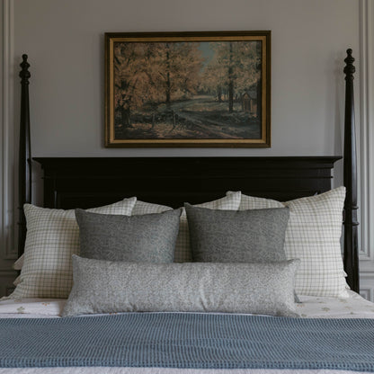 Blue lumbar pillow on bed with checkered and gray patterned pillows.