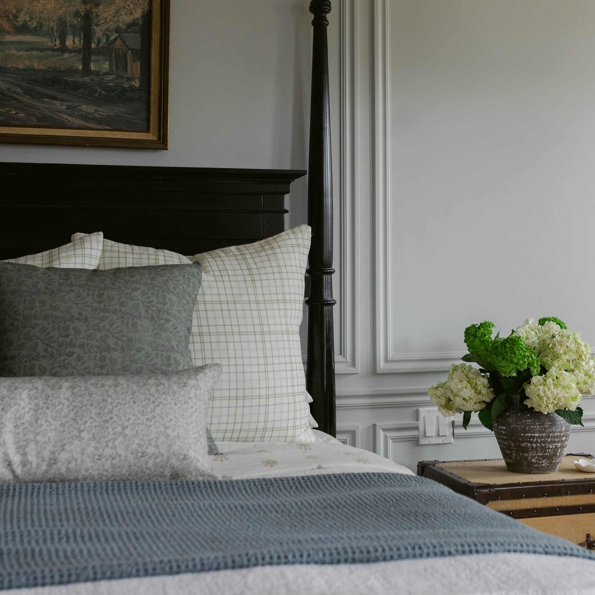 Blue textured bedspread layered with patterned pillows on a black four-poster bed.
