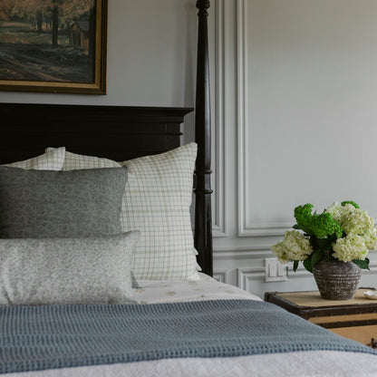Blue textured bedspread layered with patterned pillows on a black four-poster bed.