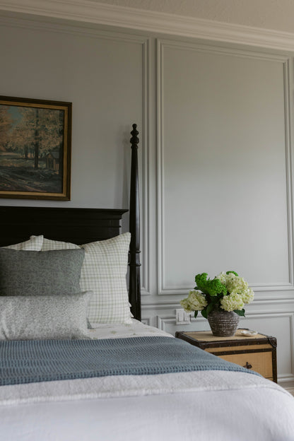 Beige linen pillow styled on a bed with white grid and gray patterned pillows.