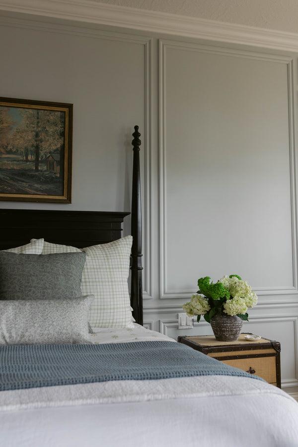 Beige linen pillow styled on a bed with white grid and gray patterned pillows.