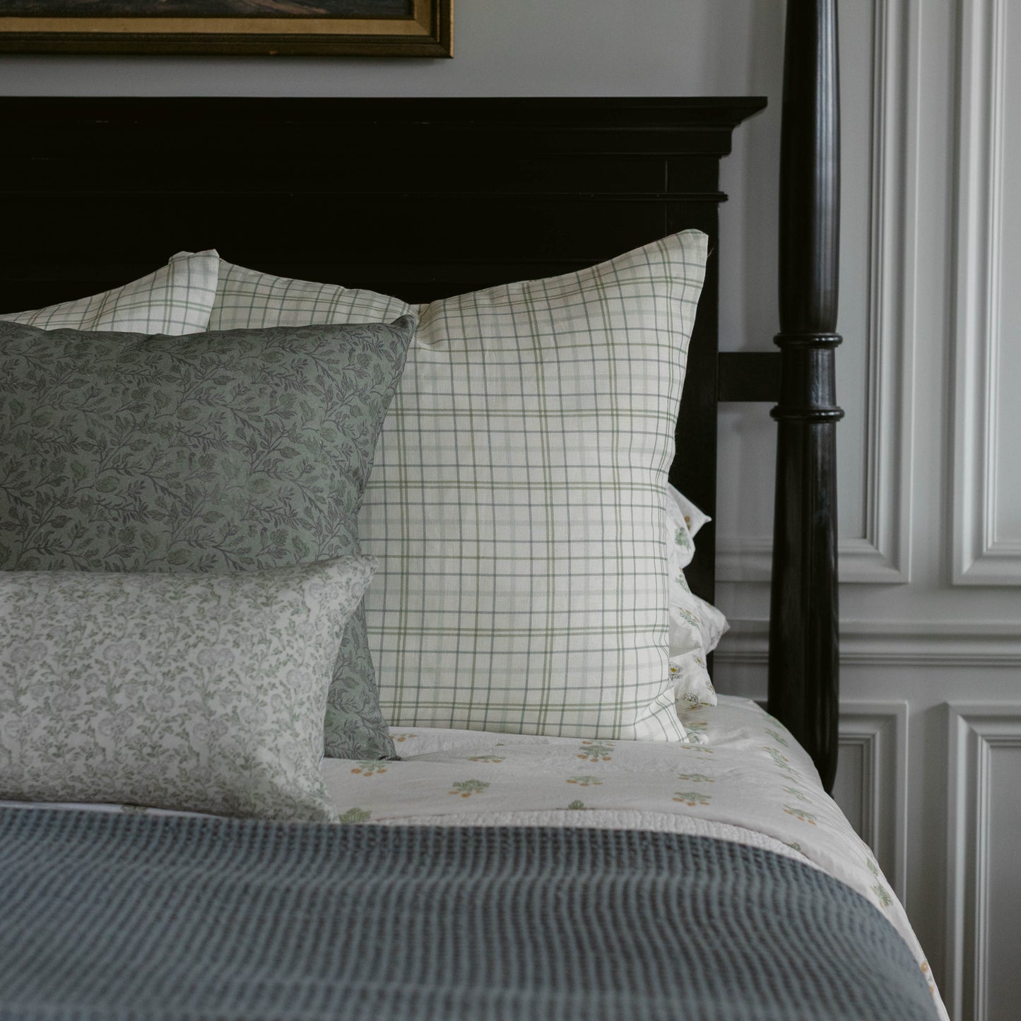 Blue and white plaid pillow on bed with floral patterned pillows and striped bedding.