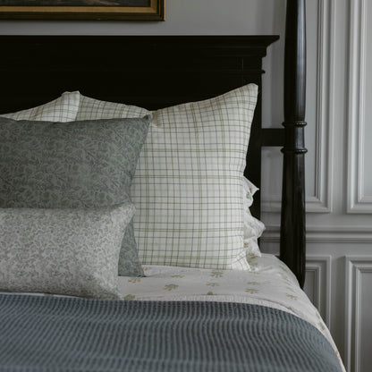 Blue and white plaid pillow on bed with floral patterned pillows and striped bedding.
