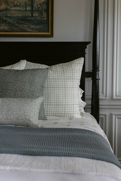 Rhodes linen pillow with green windowpane pattern displayed on black bed frame with coordinating bedding.
