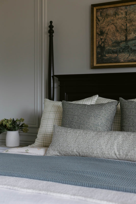Gray patterned pillows and blue textured bedding on a black metal bed frame.
