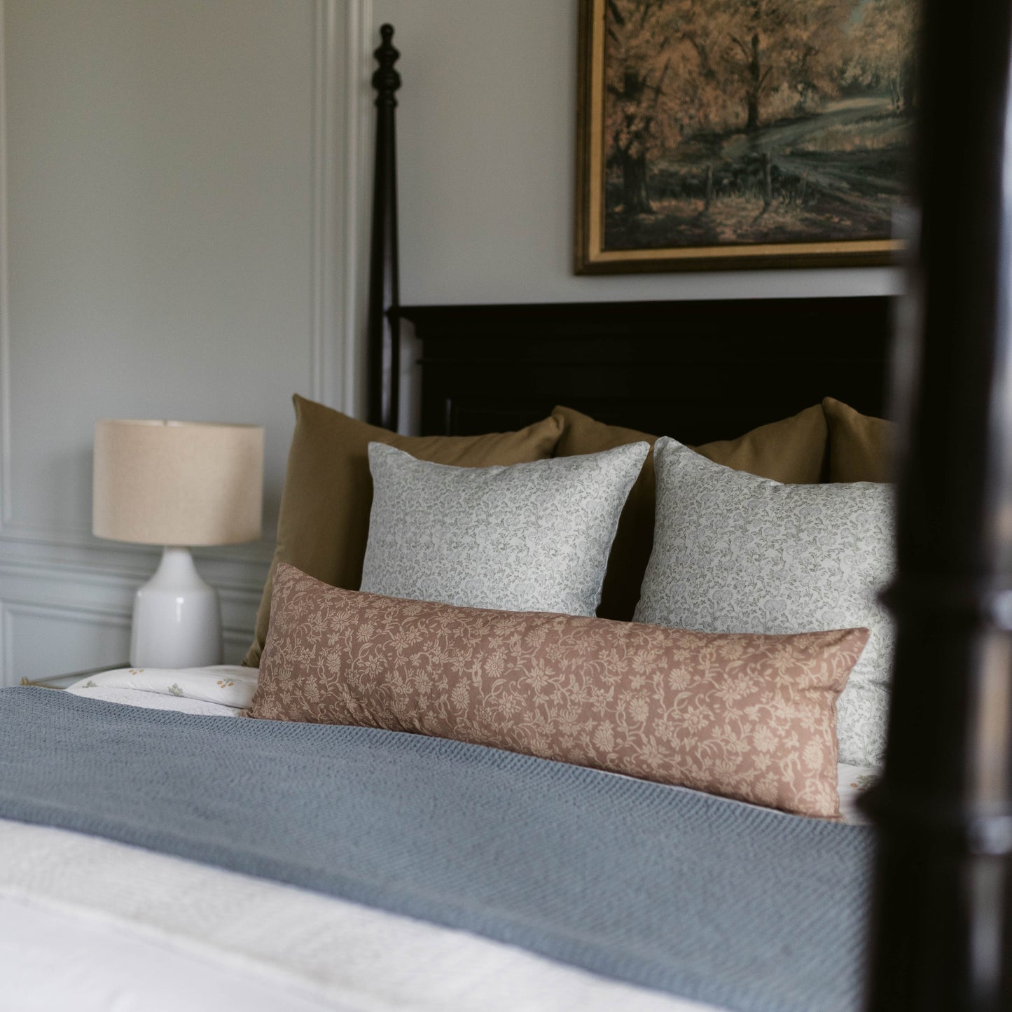 Brown patterned lumbar pillow displayed on a bed with gray and olive pillows.