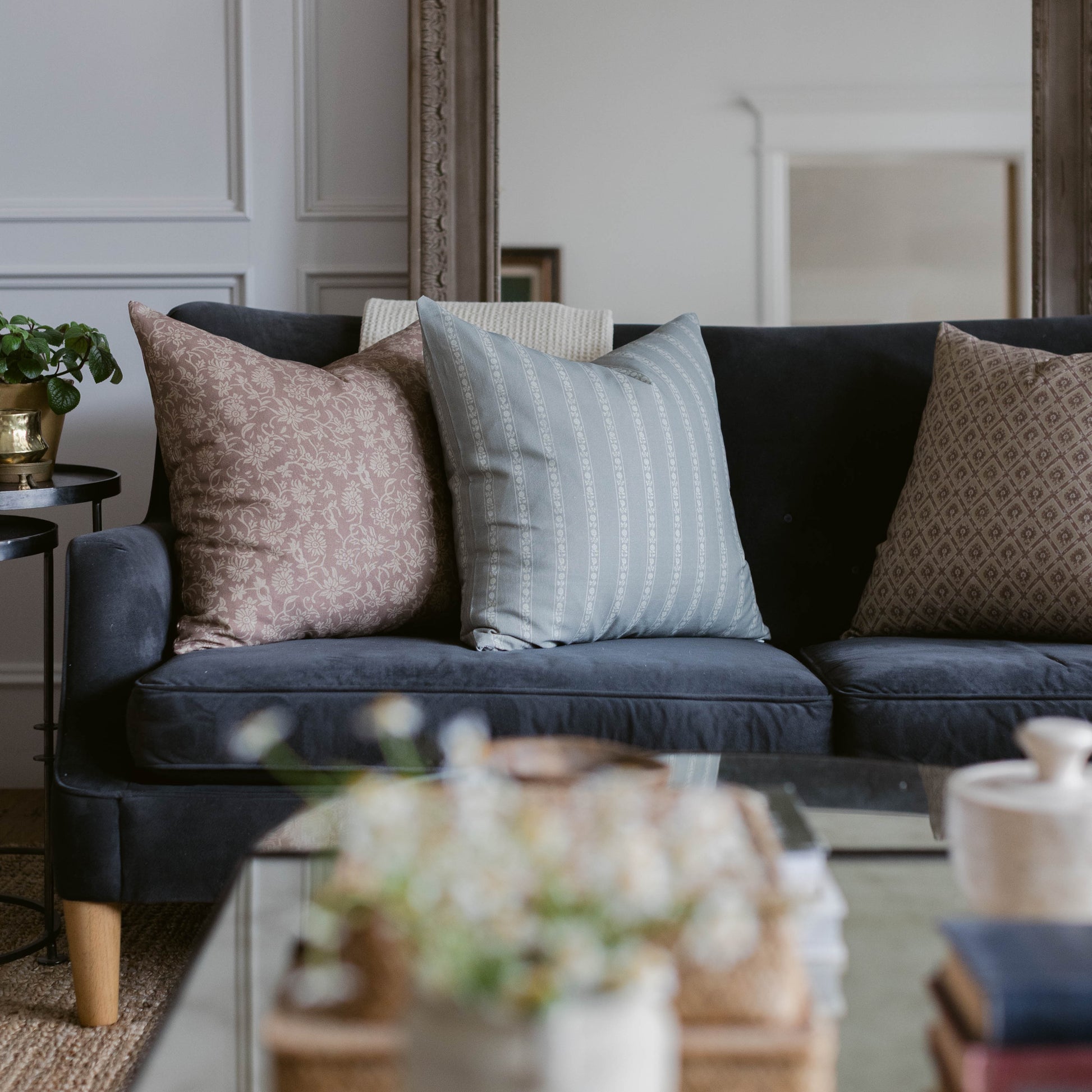 Four throw pillows in rose, light blue striped, black, and beige patterned fabrics arranged on a dark navy sofa.