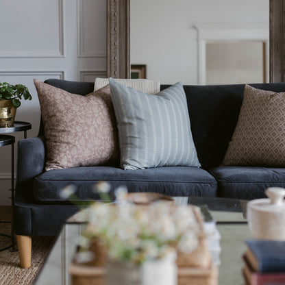 Four throw pillows in rose, light blue striped, black, and beige patterned fabrics arranged on a dark navy sofa.