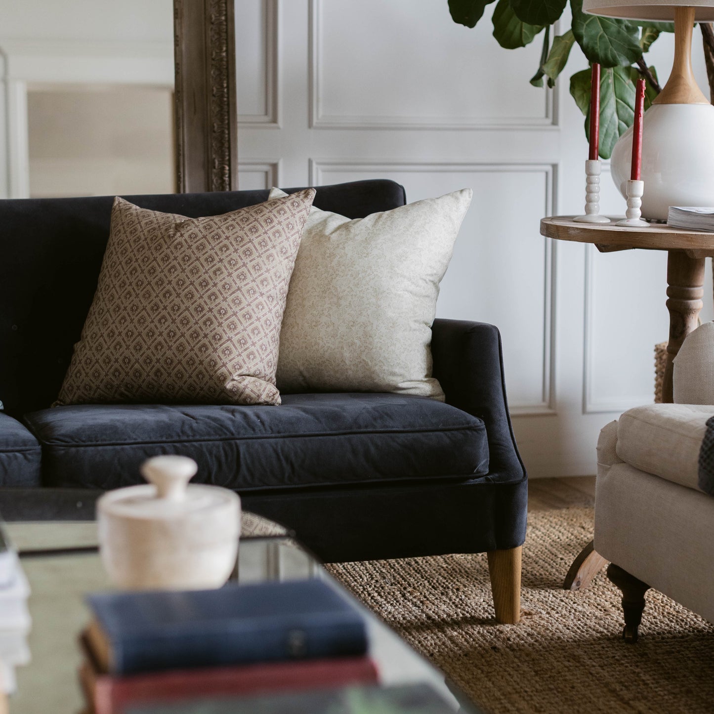 Two throw pillows on black sofa: one with geometric pattern in tan, one solid cream linen.