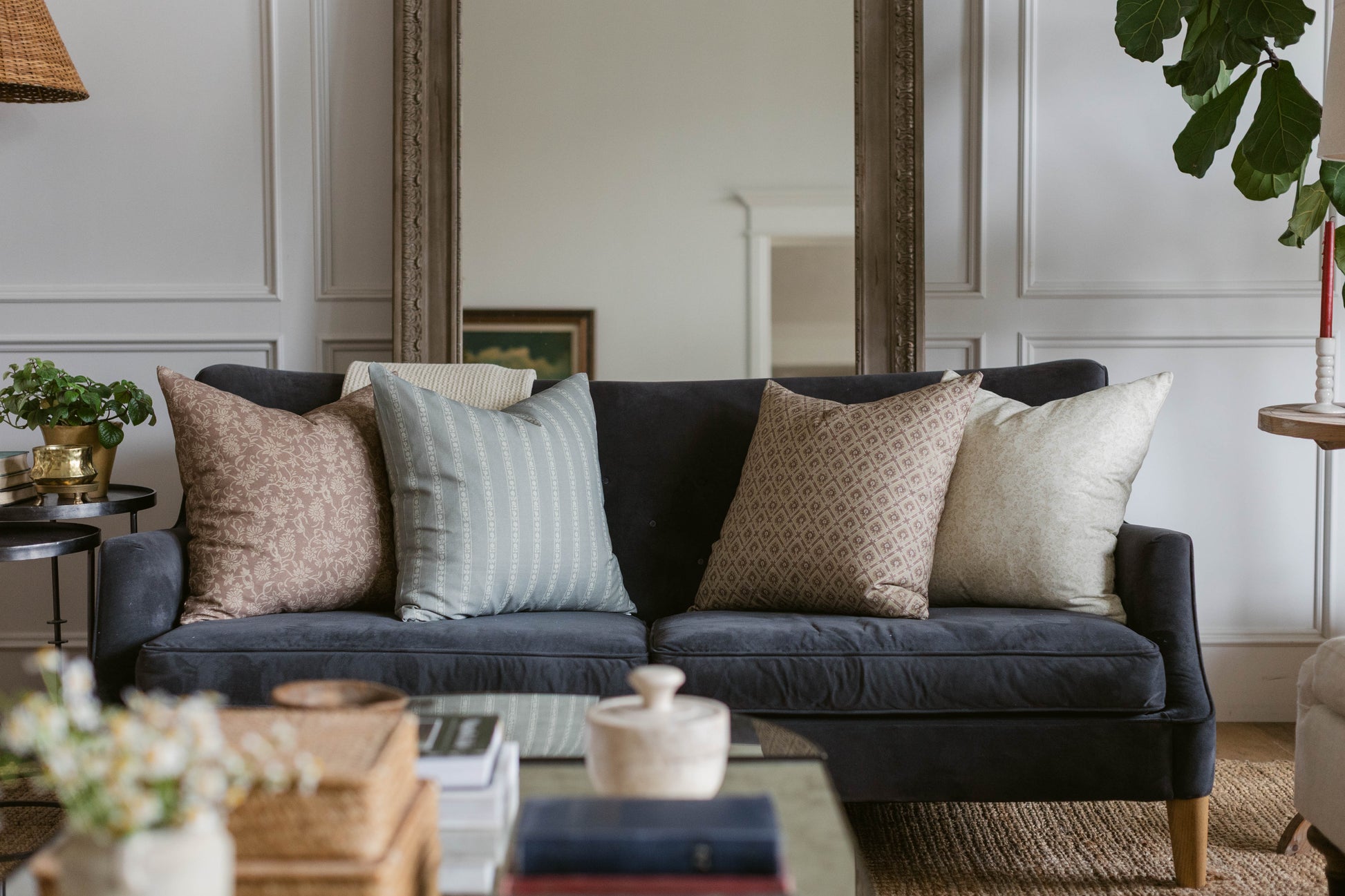 Noa throw pillow in taupe displayed on dark navy sofa with striped and textured accent pillows in living room setting.